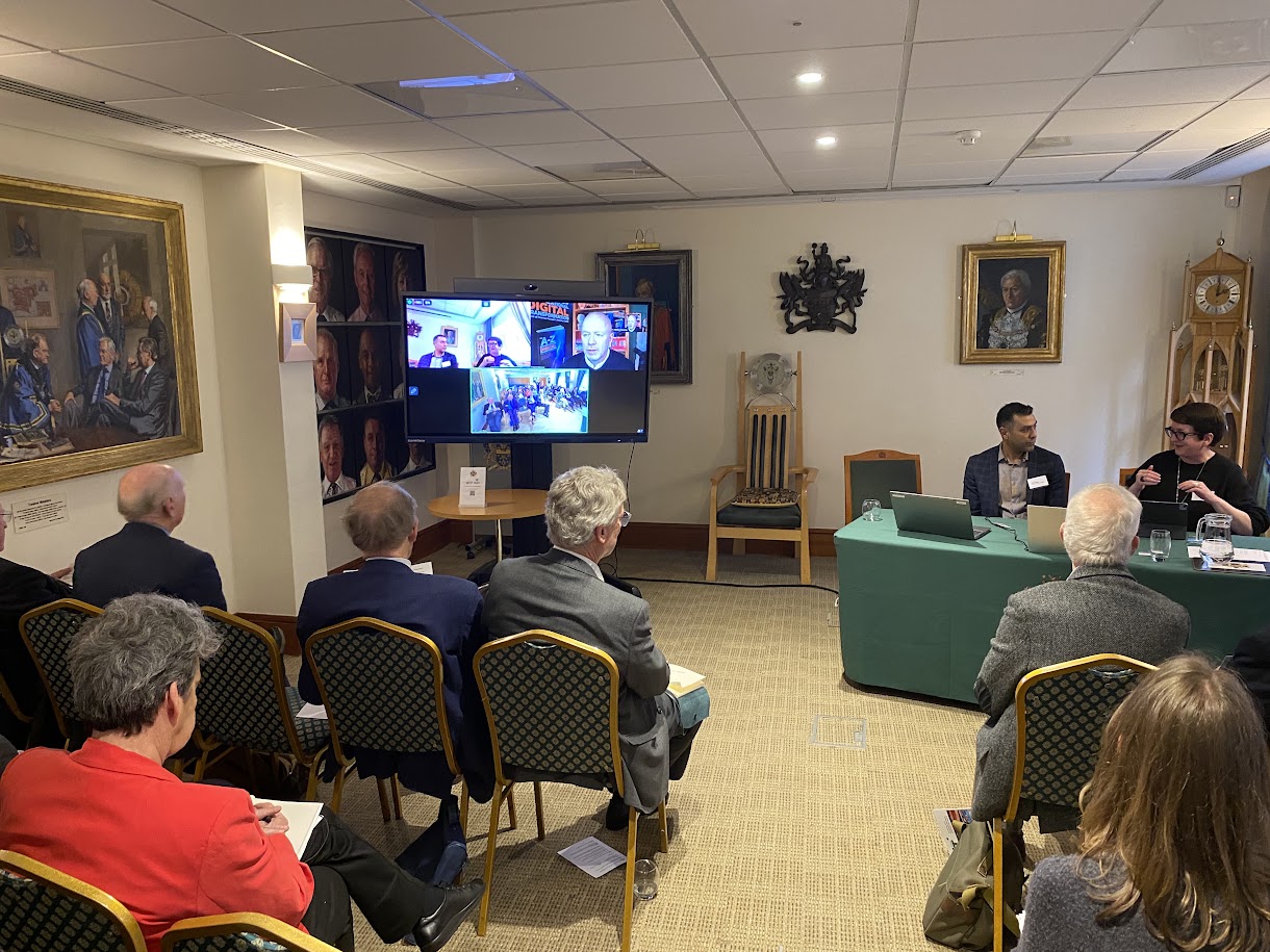 Ravi Chagger seated on the panel at WCIT, in front of the audience and speaking with a colleague